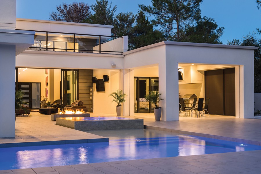 an outdoor entertainment area with a pool, TV, fireplace, and outdoor lighting